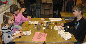 Kinder sitzen bei einem Workshop rund um einen Tisch und arbeiten