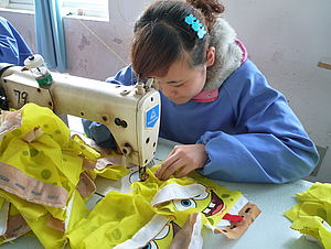 Eine Arbeiterin sitzt in einer chinesischen Fabrik und näht Spielzeug