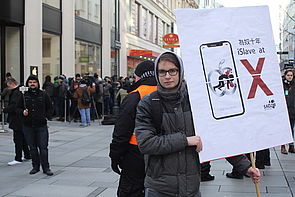 Ein Südwind-Aktivist hält vor einem Apple-Store ein den Konzern kritisierendes Schild hoch