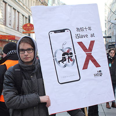 Ein Südwind-Aktivist hält vor einem Apple-Store ein den Konzern kritisierendes Schild hoch