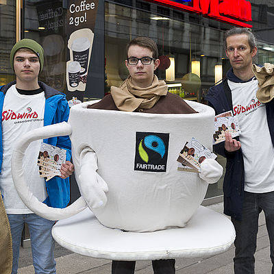 Drei junge Männer bei einer Kampagne für fairen Kaffee. Einer ist als große Kaffeetasse verkleidet