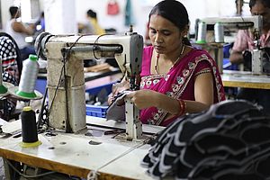 An einer großen Nähmaschine sitzt eine indische Arbeiterin und arbeitet an einem Schuh