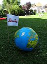 Aufgeblasener Wasserball bedruckt mit einer Weltkarte, daneben steckt im Boden eine Südwind Fahne