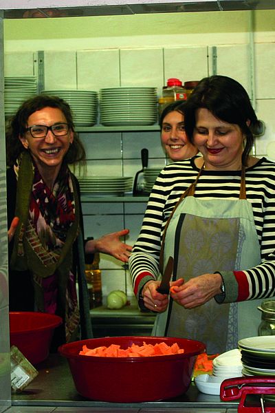 Drei Frauen bereiten in einer Küche Essen vor, lachen dabei in die Kamera