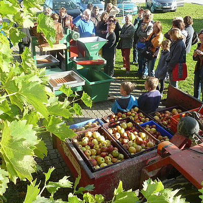 Ansammlung mehrerer Menschen im Freien. Daneben Kisten gefüllt mit Äpfeln 