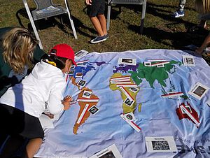 Kinder erforschen auf einer Weltkarte aus Stoff die Abbauländer von Rohstoffen für die Elektronikproduktion