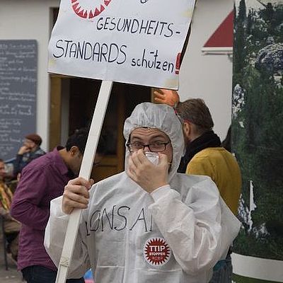 Ein in Schutzanzug Protestierender hält ein Schild gegen TTIP in die Luft