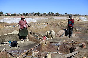 Zwei ArbeiterInnen beim Zinnabbau in Bolivien. Die beiden stehen auf einer großen, umgegrabenen Fläche