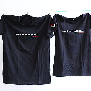 Zwei aufgehängte, schwarze T-Shirts. In weiß darauf gedruckt "weltverbesserIn"