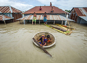 Menschen schützen sich vor einem Hochwasser in Sirajganj, Bangladesch, ein Haus steht fast unter Wasser, Familienmitglieder flüchten auf das Dach und in einem kleinen Schlauchboot