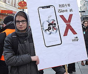 Ein Südwind Aktivist macht mit einem Schild auf die miserablen Arbeitsbedingungen beim Konzern Apple aufmerksam