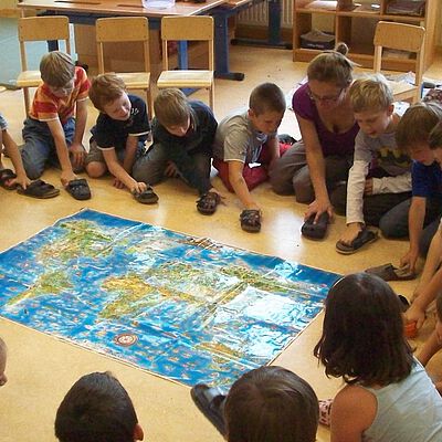 Viele Kinder bilden einen Sitzkreis rund um eine Weltkarte. Projekt Kakao für Minis 
