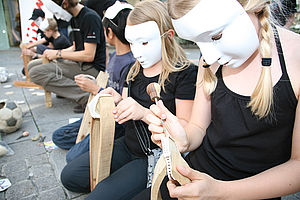 Südwind AktivistInnen nähen mit weißen Masken Fußbälle auf öffentlichen Plätzen. So wollen sie auf das Problem aufmerksam machen