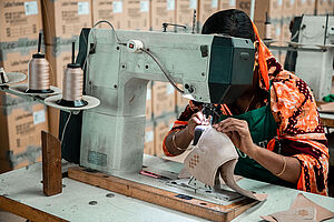 In Sari gekleidete Frau betätigt eine Nähmaschin in einer Textilfabrik in Bangladesch für Lederwaren und Schuhe
