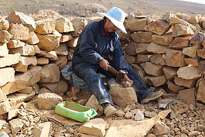 Arbeiter beim Kleinbergbau in Bolivien. Er sitzt neben einer Mauer aus aufgestapelten Steinen