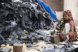 Einer Arbeiterin in Indien sitzt neben einem großen Berg Material am Boden und stellt Teile für Schuhe her