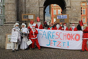 Südwind AktivistInnen als Nikolos verkleidet halten ein Banner mit dem Text "Faire Schoko jetzt!"