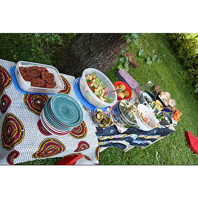 Tische mit Essen auf einer Wiese. Im Hintergrund Sitzkissen am Boden