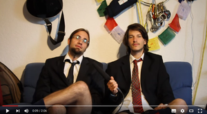Screenshot YouTube-Video "AktivistInnen Salzburg". Zwei junge Männer sitzen mit einem Mikrofon auf einem Sofa