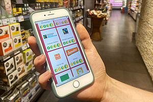 Eine Hand hält ein Handy im Supermarkt mit dem Labelcheck am Bildschirm