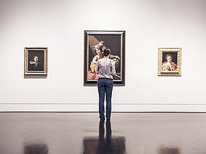 Eine Frau steht bei einer Ausstellung vor einer Wand und betrachtet die aufgehängten Bilder