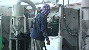 Ein Arbeiter in einer Fabrik zur Jeans-Herstellung. Zum Schutz seiner Atemwege hat er ein Stück Stoff um den Hals gewickelt