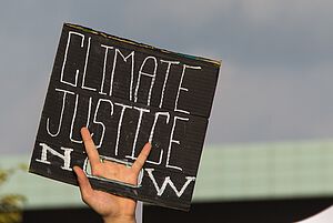 Eine protestierende Person hält ein Schild mit den Worten "climate justice now" in die Höhe