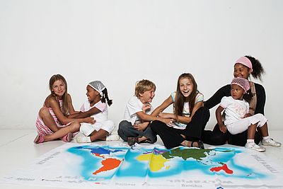 Kinder sitzen vor einer Weltkarte am Boden 