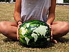 Zwei Hände halten eine Wassermelone. Auf ihrer Oberfläche ist die Weltkarte eingeritzt.