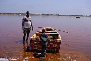 Salzbauer und Kind stehen im Wasser vor einem Holzboot