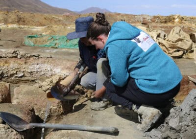 Zinnabbau in Machacamarca in Bolivien: Zwei Personen hocken in einer kargen Gegend auf dem Boden über Werkzeuge gebeugt Zinnabbau in Machacamarca in Bolivien-