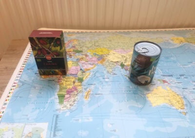 Ausstellungsobjekte von Map your Ice Cream: Eine Weltkarte, auf der eine Packung Kakao und eine Dose Kokosmilch abgestellt sind