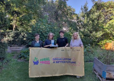 2 Preisträgerinnenn und zwei Mitarbeiterinnen stehen im Garten mit der Projektfahne.
