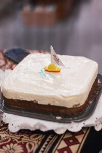 Ein Kuchen mit weißer Creme und einem kleinen Segelboot oben drauf.