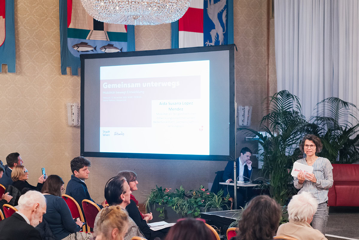 Moderatorin spricht vor einer Leinwand zu Publikum im Wiener Rathaus